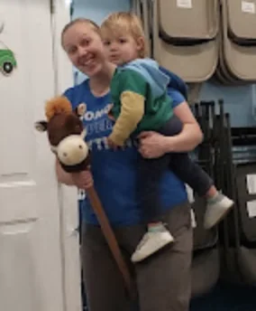 A grown-up holding a toddler and a hobby-horse in class