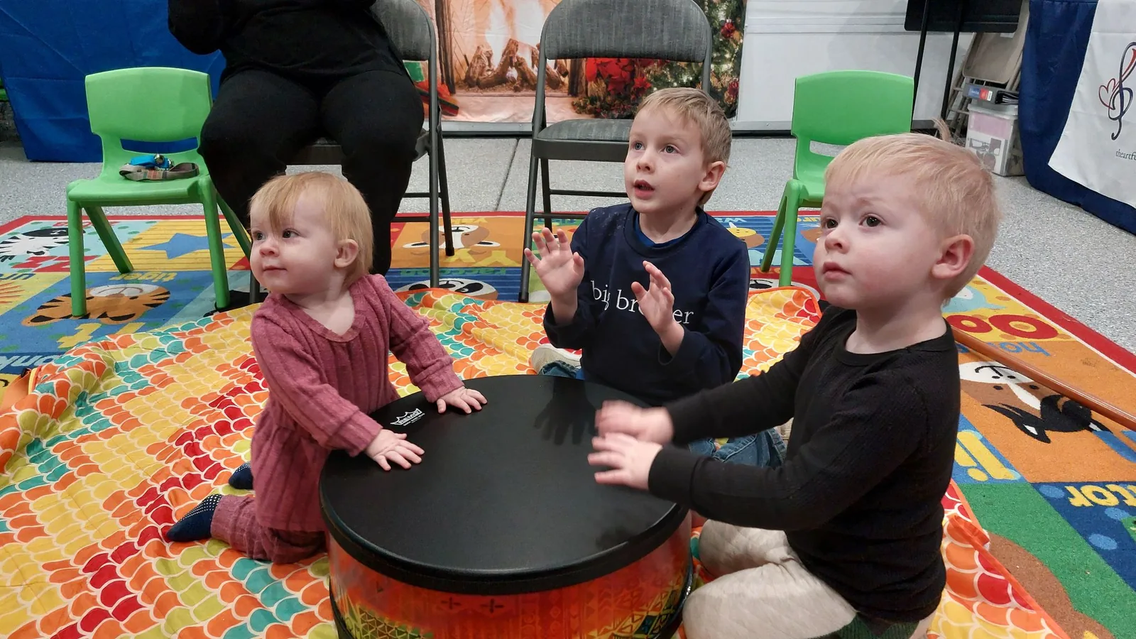 Toddlers playing a hand drum together on the floor